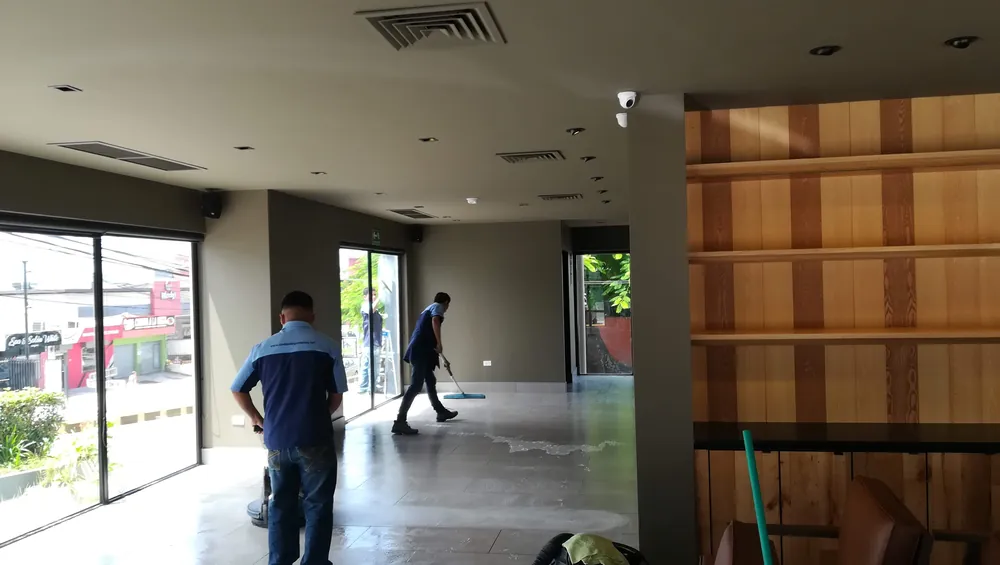Técnicos limpiando piso y vidrios con equipo especializado en un local comercial recién construido
