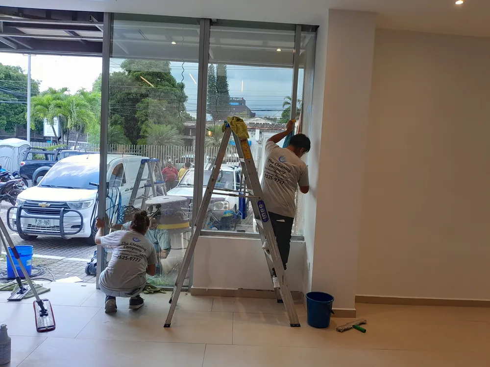 Técnicos limpiando vidrios de fachada con escuadra y cubeta